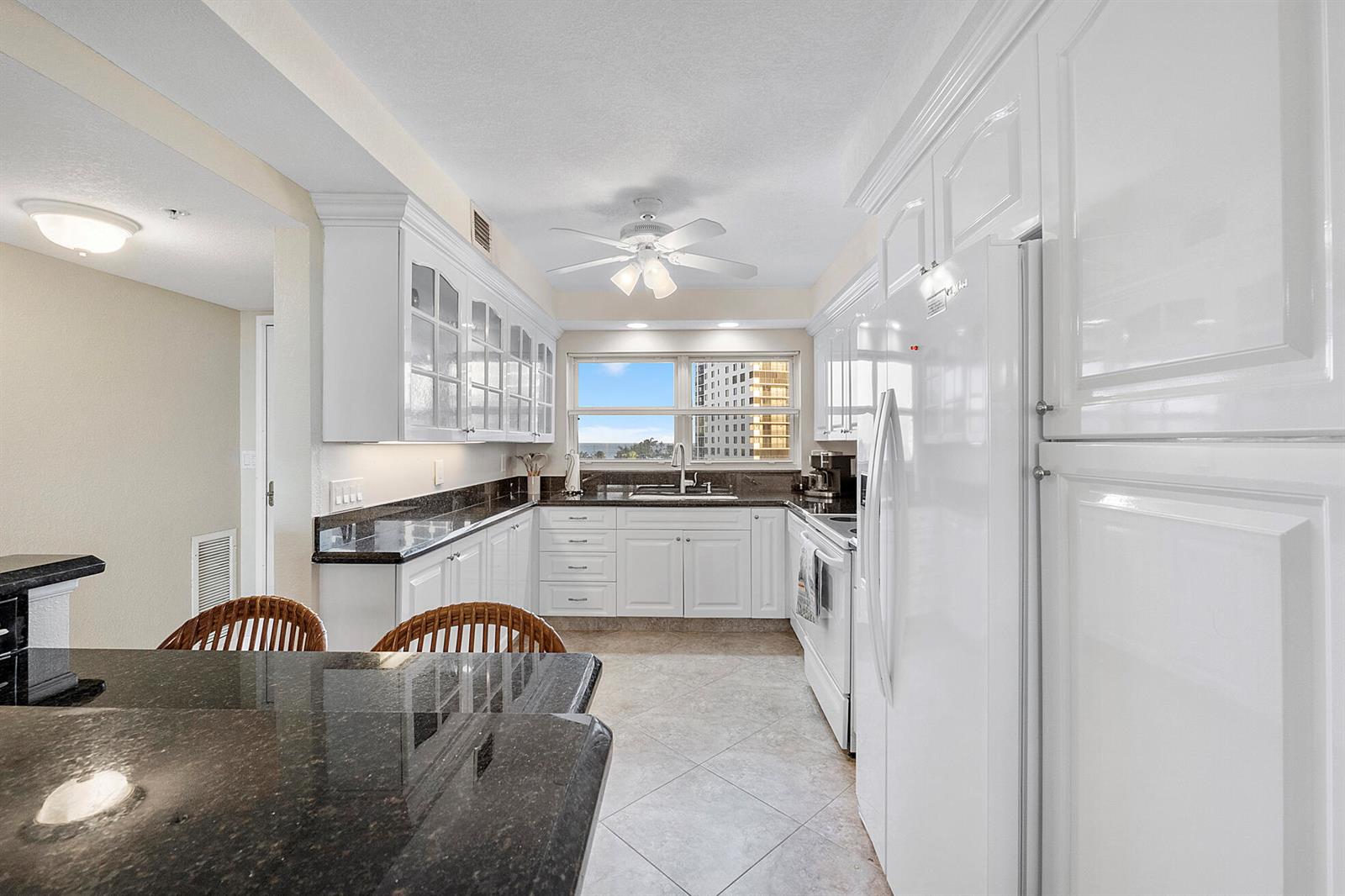 A white kitchen features dark granite countertops, a ceiling fan, and a view of buildings — 3310 S Ocean Boulevard # d, Highland Beach FL 33487, HIGHLAND BEACH, FL
