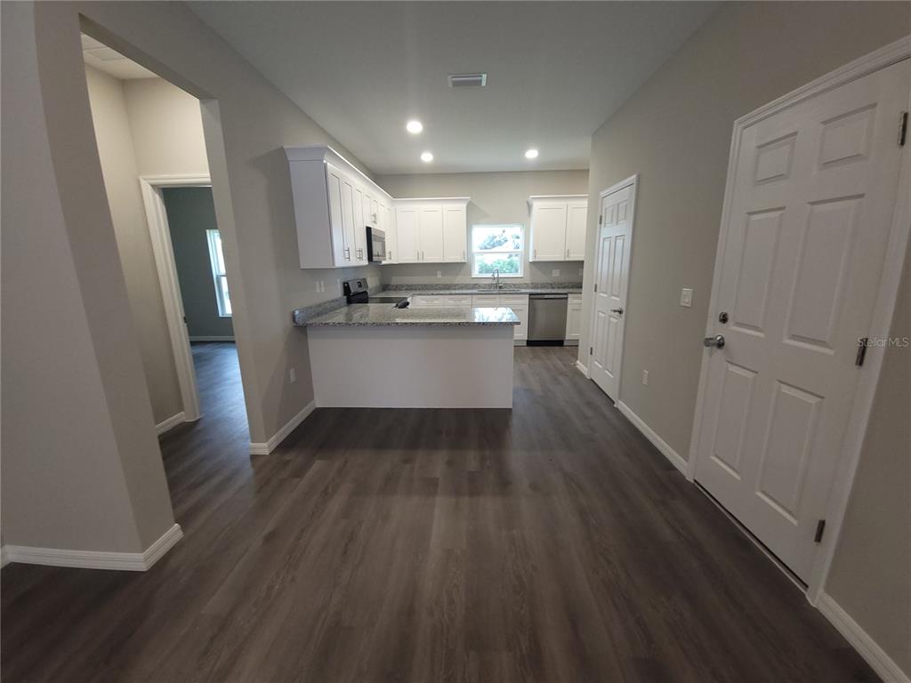 A kitchen with white cabinets, granite countertops, and wood-look flooring opens to a living area — 5025 FINDERS COURT, TAMPA, FL