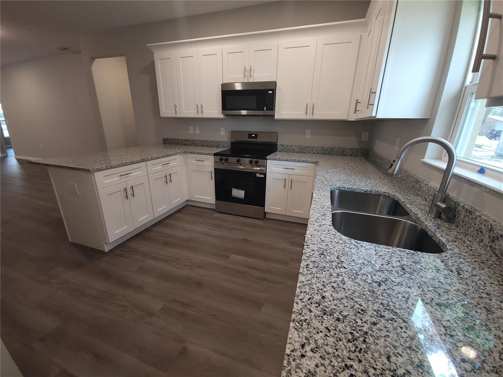 A kitchen features white cabinets, granite countertops, stainless steel appliances, and wood-look flooring — 5025 FINDERS COURT, TAMPA, FL