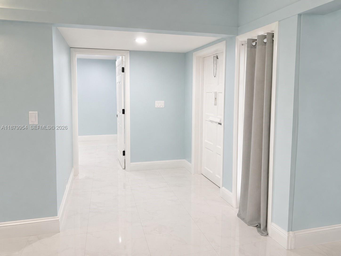 A hallway with light blue walls, white tile flooring, and two white interior doors — 4713 Holly Dr, Tamarac FL 33319, TAMARAC, FL