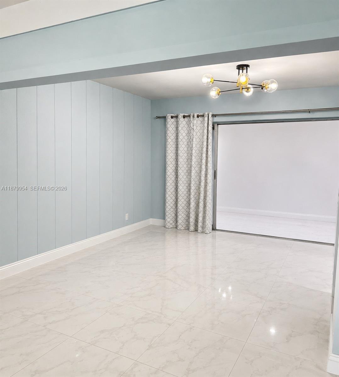 A room with light blue vertical paneling, white marble-look tile floors, and a modern chandelier — 4713 Holly Dr, Tamarac FL 33319, TAMARAC, FL