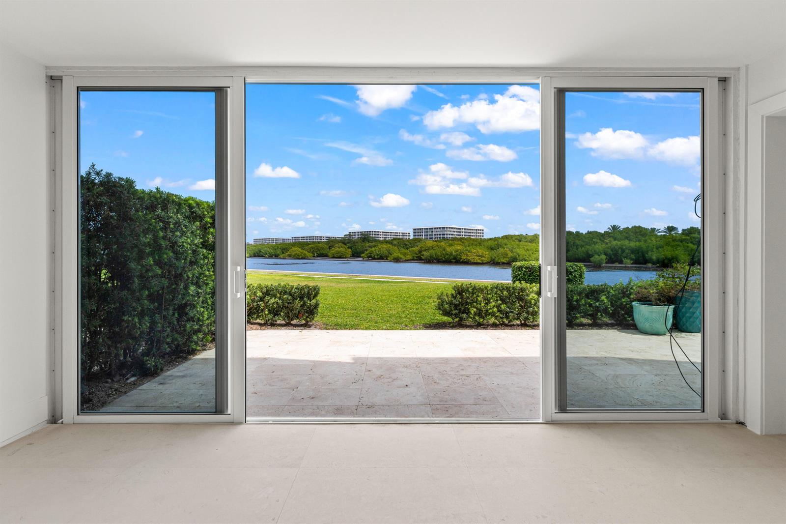A room with large sliding glass doors looking out onto a patio, lawn, and water — 2185 Ibis Isle Road # 1, Palm Beach FL 33480, PALM BEACH, FL