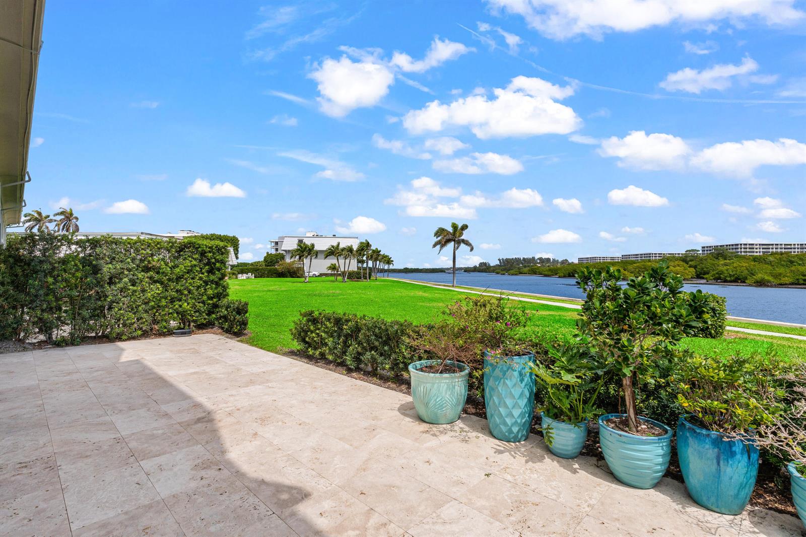 A stone patio overlooks a grassy lawn, a waterway, and a distant building — 2185 Ibis Isle Road # 1, Palm Beach FL 33480, PALM BEACH, FL