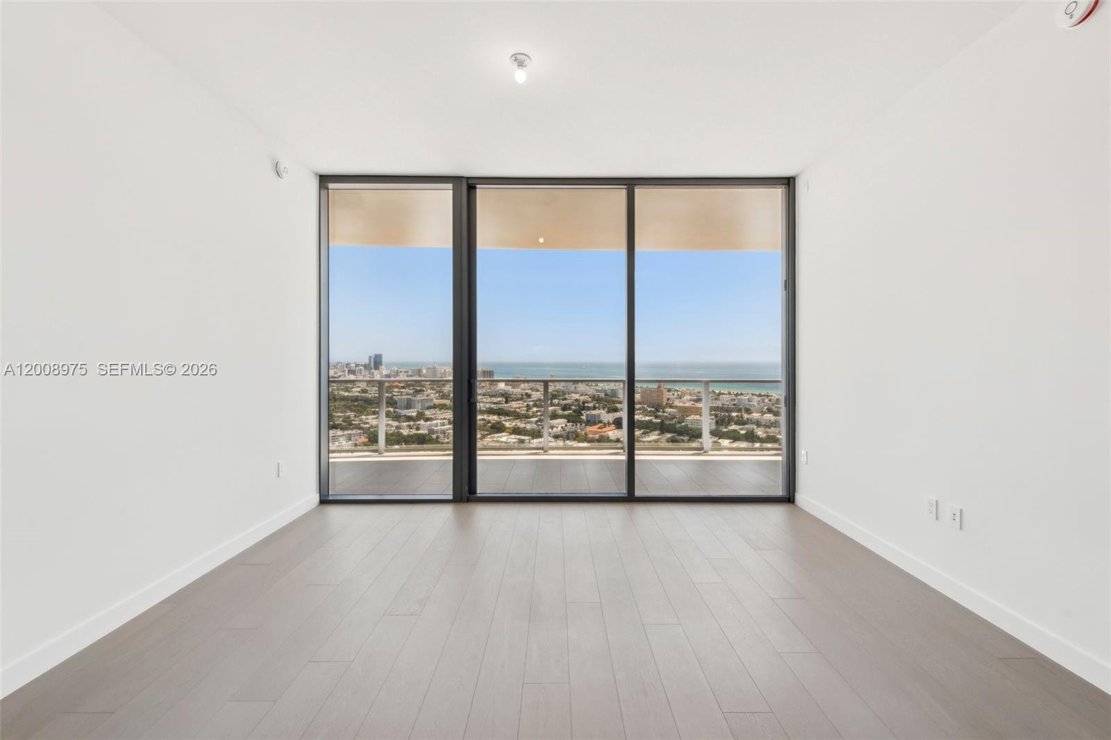 An empty room features light wood flooring, white walls, and floor-to-ceiling windows overlooking the ocean — 500 Alton Rd. # 3004, Miami Beach FL 33139, MIAMI BEACH, FL