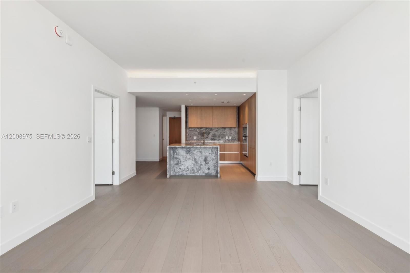 A modern kitchen with a marble island and wood cabinetry sits at the end of an open-plan room — 500 Alton Rd. # 3004, Miami Beach FL 33139, MIAMI BEACH, FL