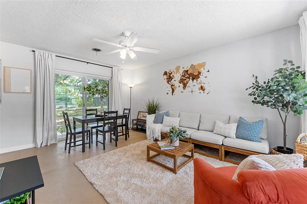A living and dining room features a sectional sofa, wooden coffee table, and world map wall art — 205 WILSHIRE DRIVE, CASSELBERRY, FL