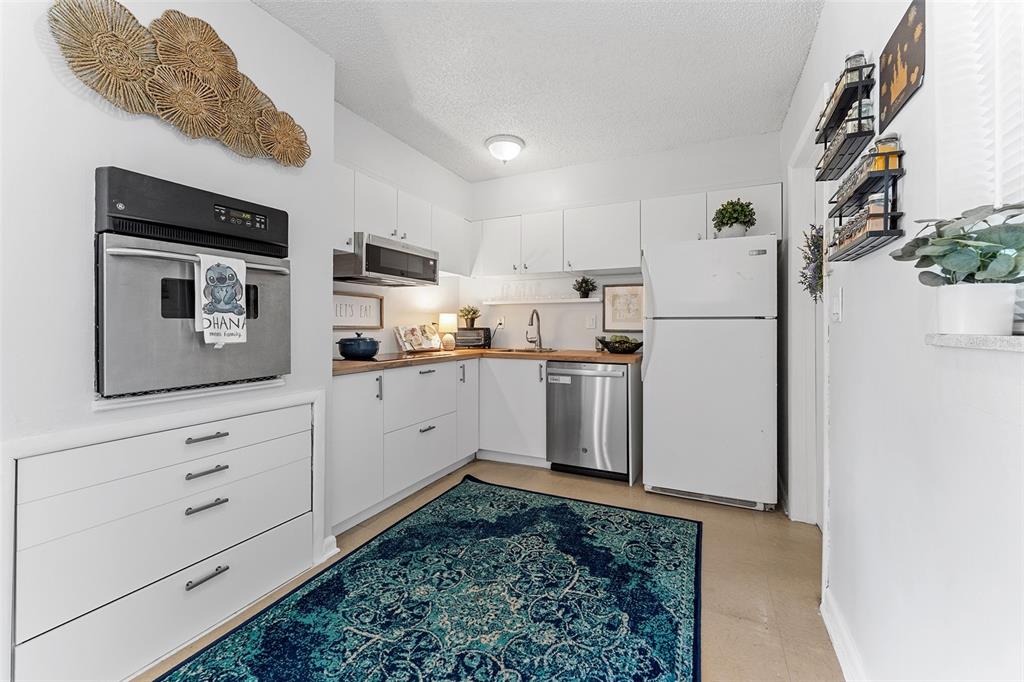 A kitchen features white cabinets, stainless steel appliances, wood countertops, and a blue patterned rug — 205 WILSHIRE DRIVE, CASSELBERRY, FL