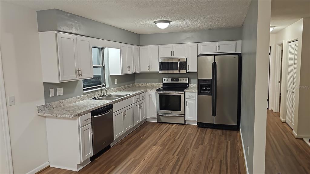 A kitchen with white cabinets, stainless steel appliances, and wood-look flooring — 6862 SE 52 PLACE, OCALA, FL