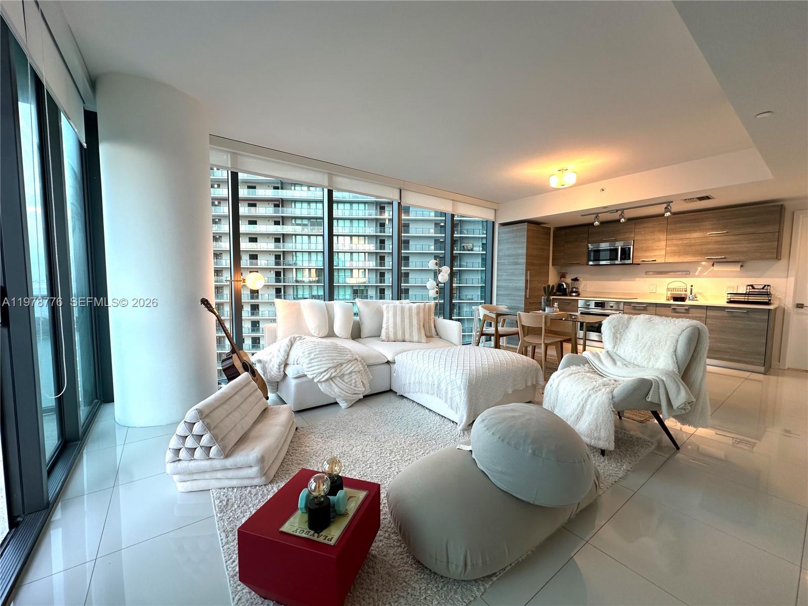 A modern living room with white tile floors, a sectional sofa, and an open kitchen — 650 NE 32nd St # 2108, Miami FL 33137, MIAMI, FL