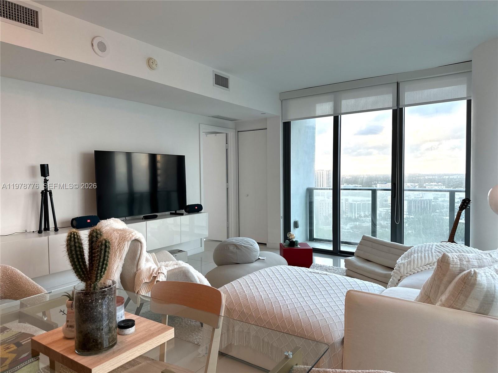 A modern living room features a large television, white furniture, and floor-to-ceiling windows with views — 650 NE 32nd St # 2108, Miami FL 33137, MIAMI, FL
