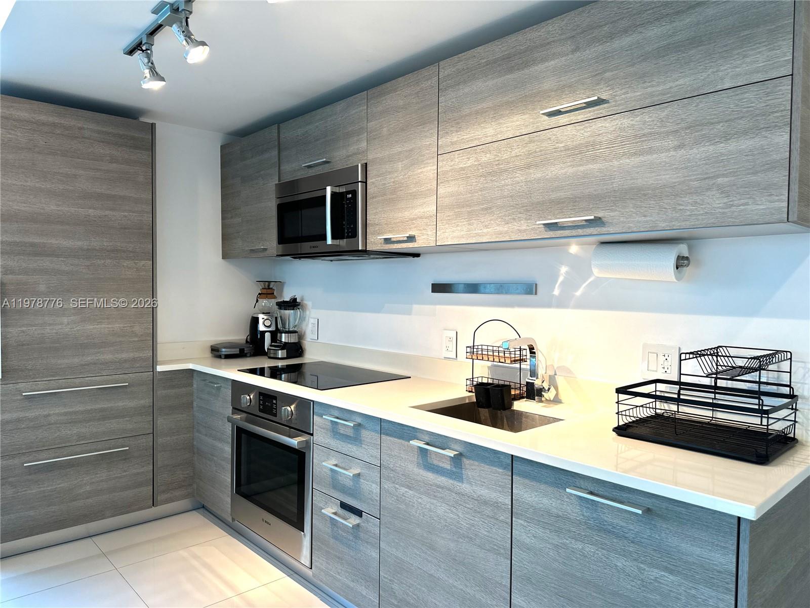 A modern kitchen features gray wood-grain cabinets, stainless steel appliances, and white countertops — 650 NE 32nd St # 2108, Miami FL 33137, MIAMI, FL