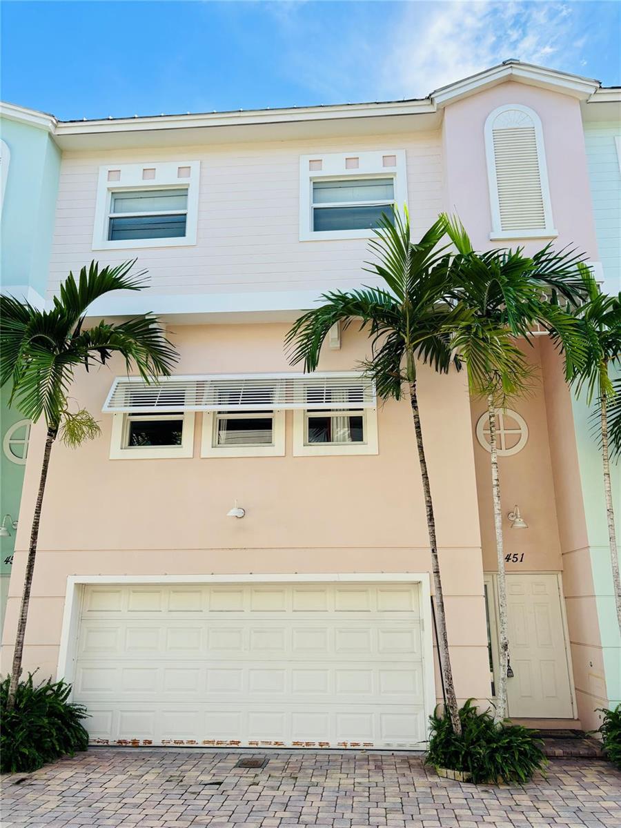 A three-story townhouse with pastel siding, a two-car garage, and palm trees in front — 451 NE 1st Street # 451, Pompano Beach FL 33060, POMPANO BEACH, FL