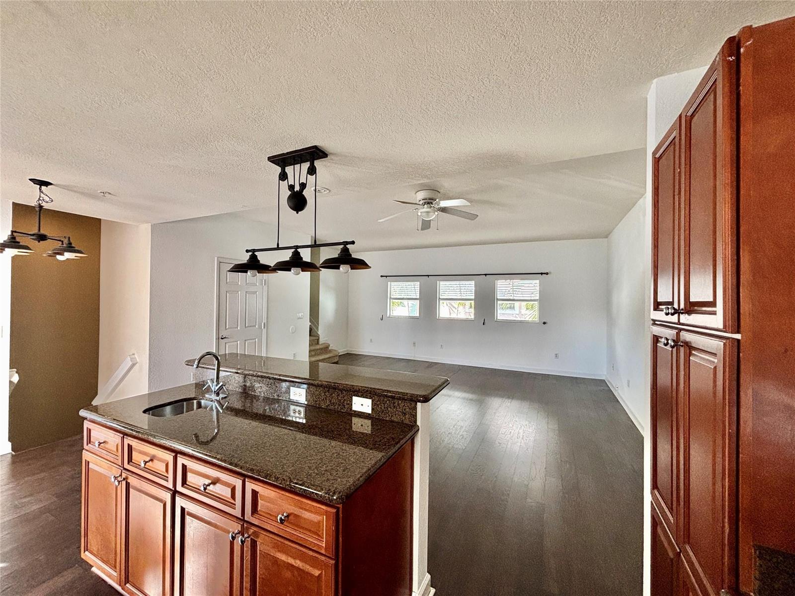 A kitchen island with granite countertops overlooks an open living area with hardwood floors — 451 NE 1st Street # 451, Pompano Beach FL 33060, POMPANO BEACH, FL