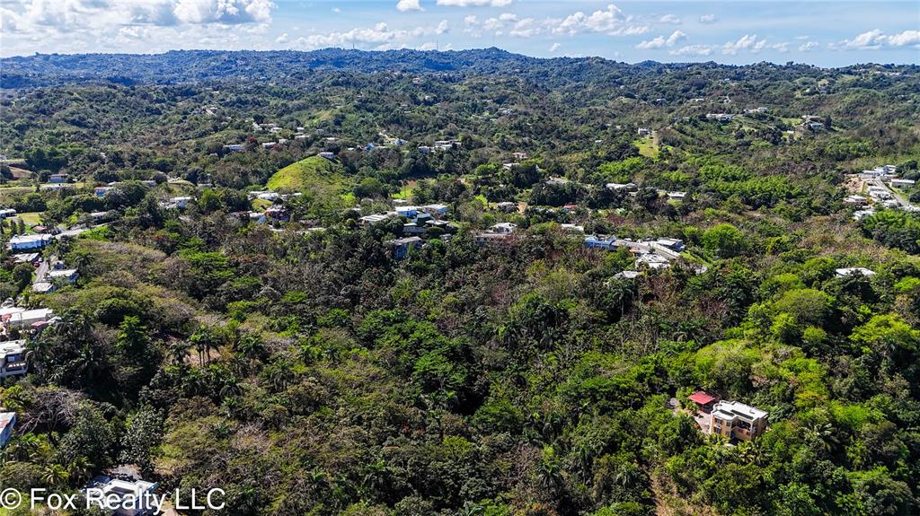An aerial view shows a house nestled in a lush, hilly, and forested landscape — Carr. 414 KM 3.2 BO.CRUCES, AGUADA, PR