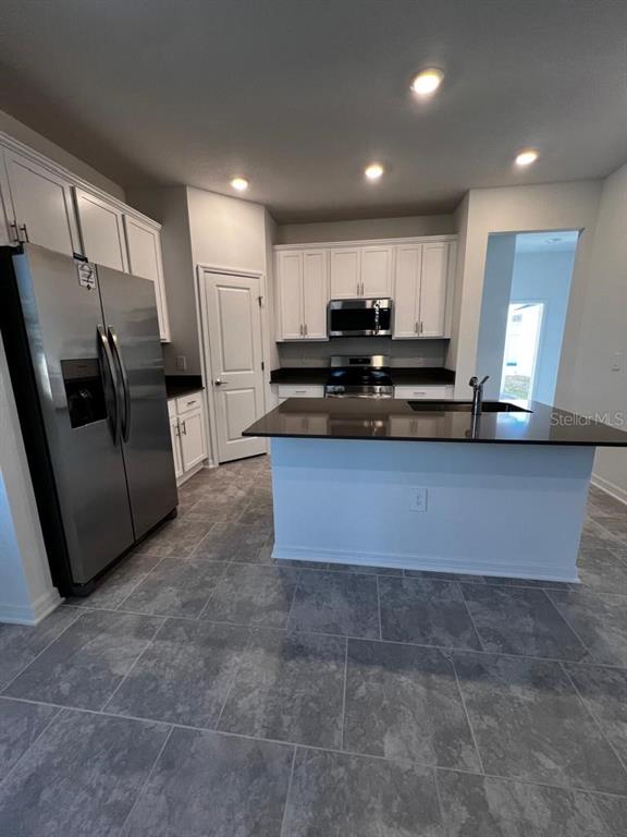 A kitchen features white cabinets, stainless steel appliances, a dark countertop island, and gray tile flooring — 4134 PINO STREET, APOPKA, FL