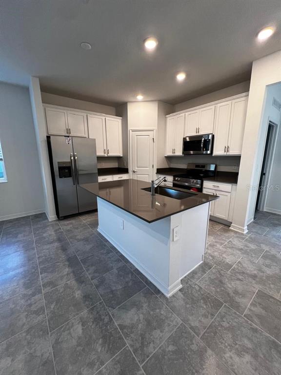 A kitchen features white cabinets, stainless steel appliances, a dark countertop island, and gray tile — 4134 PINO STREET, APOPKA, FL