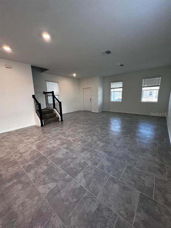 An open living area features gray tile flooring, recessed lighting, and a staircase with black railings — 4134 PINO STREET, APOPKA, FL