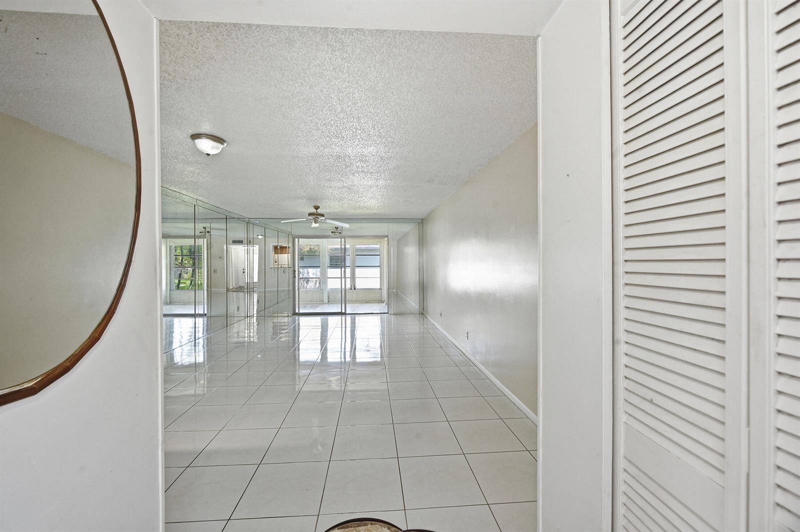 A bright, tiled living area features a mirrored wall and a ceiling fan — 6525 S Oriole Boulevard, Delray Beach FL 33446, DELRAY BEACH, FL