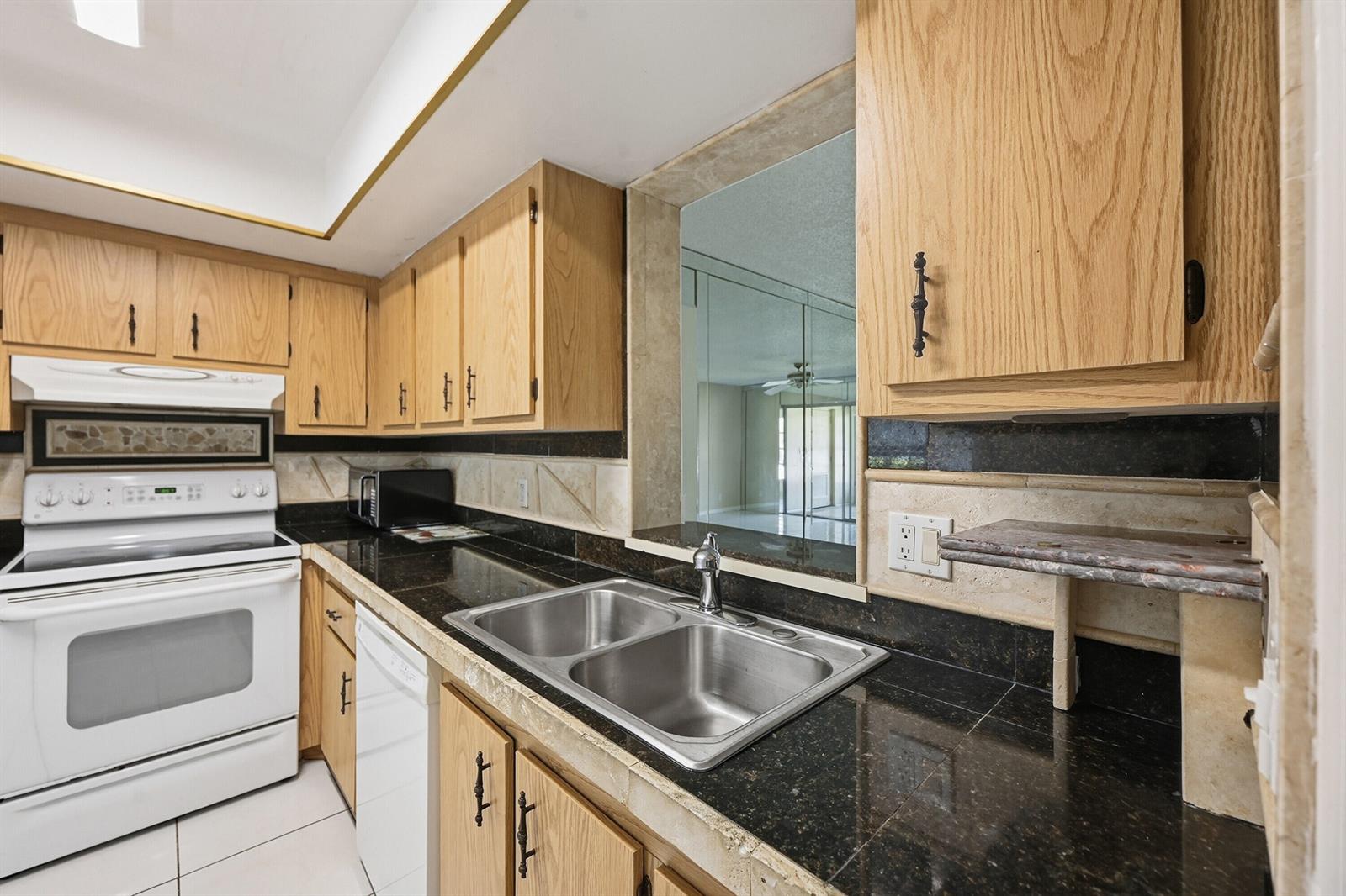 A kitchen features oak cabinets, black granite countertops, a double sink, and a pass-through window — 6525 S Oriole Boulevard, Delray Beach FL 33446, DELRAY BEACH, FL