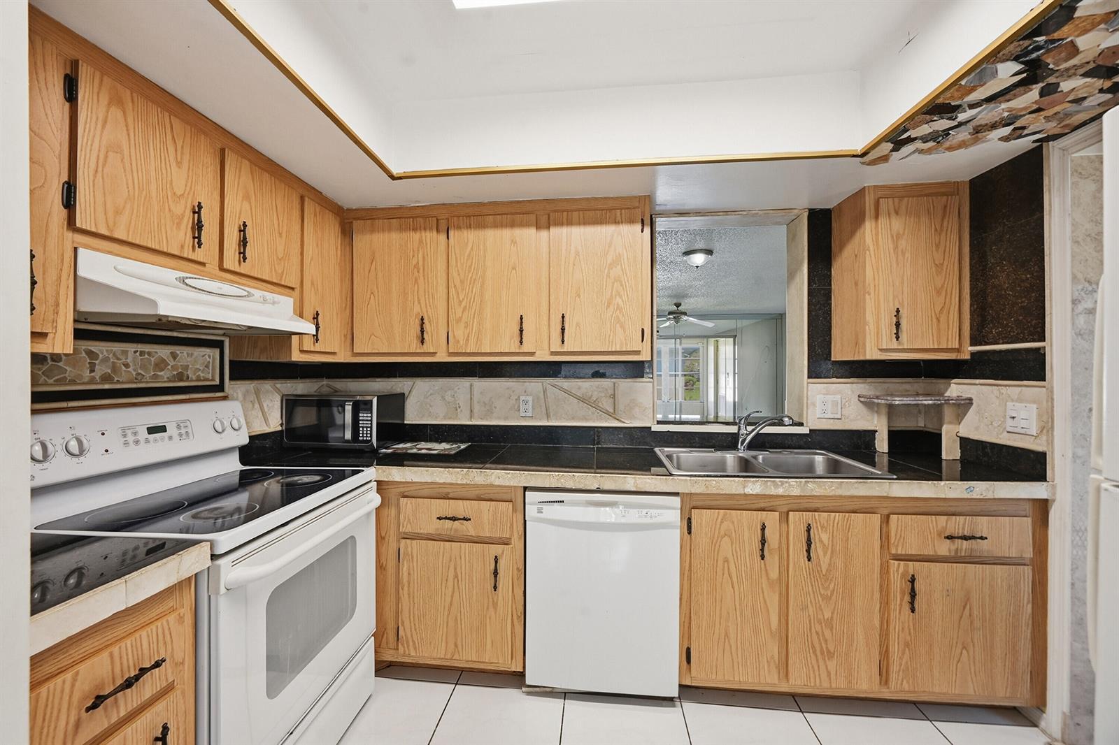 A kitchen features light wood cabinets, black countertops, a white stove, and a white dishwasher — 6525 S Oriole Boulevard, Delray Beach FL 33446, DELRAY BEACH, FL