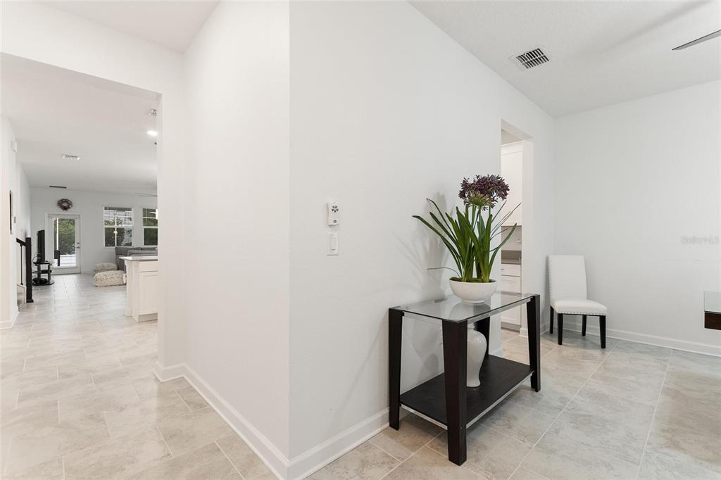 A white-walled hallway features a glass-topped console table, a potted plant, and tiled flooring — 1380 OLYMPIC CLUB BOULEVARD, CHAMPIONS GATE, FL