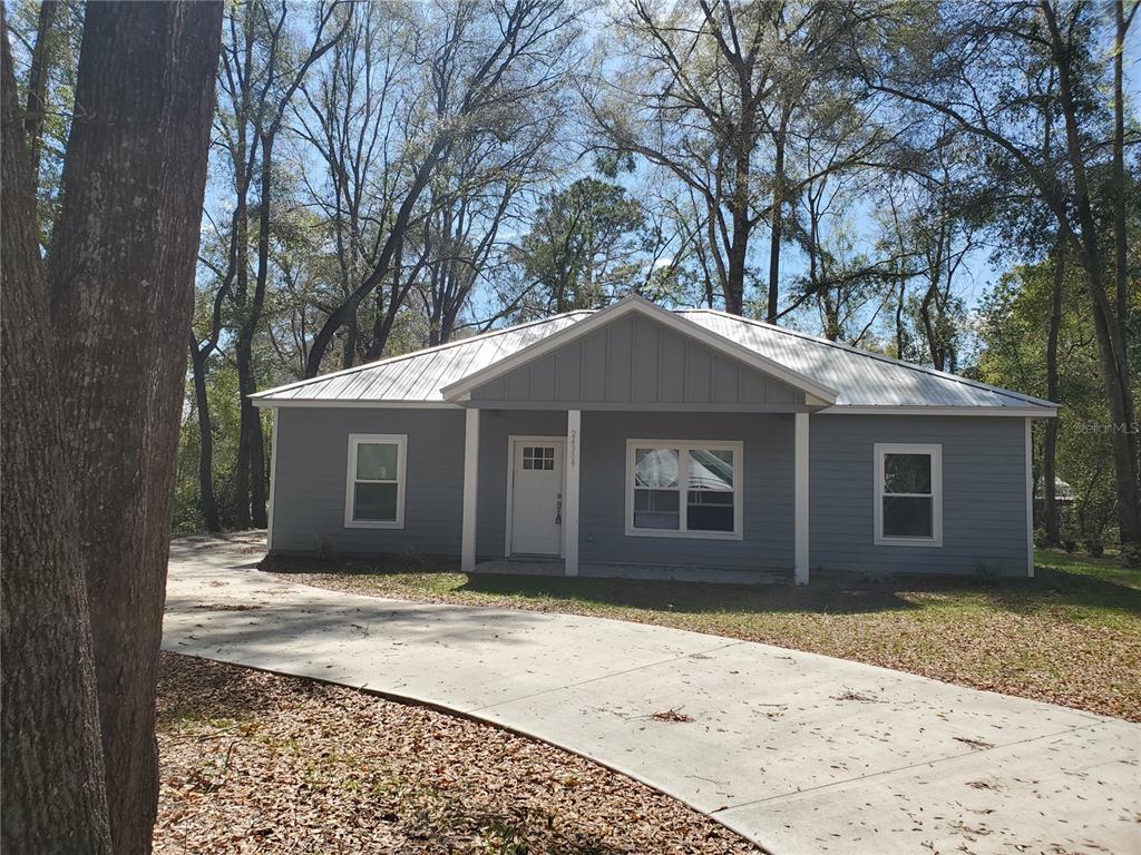 A gray, single-story house with a metal roof sits behind a concrete driveway — 24309 NW 189TH AVENUE, HIGH SPRINGS, FL