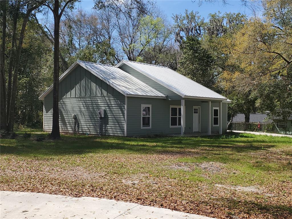 A light green house with a metal roof sits on a grassy lot with trees — 24309 NW 189TH AVENUE, HIGH SPRINGS, FL