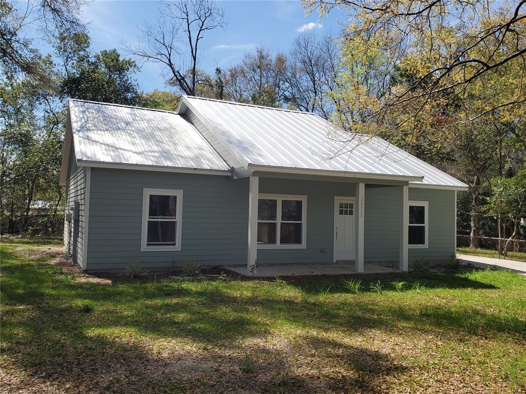 A single-story house with gray siding and a white metal roof features a front porch — 24309 NW 189TH AVENUE, HIGH SPRINGS, FL