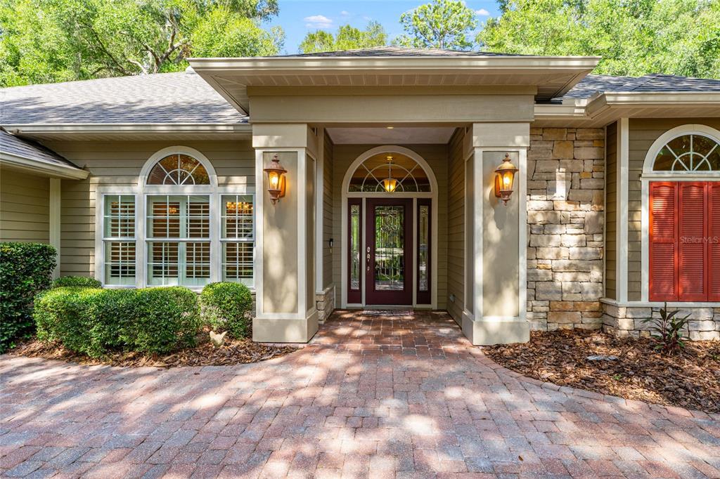 A front entrance with a stone facade, red shutters, and a brick paver walkway — 6415 SW 88TH TERRACE, GAINESVILLE, FL