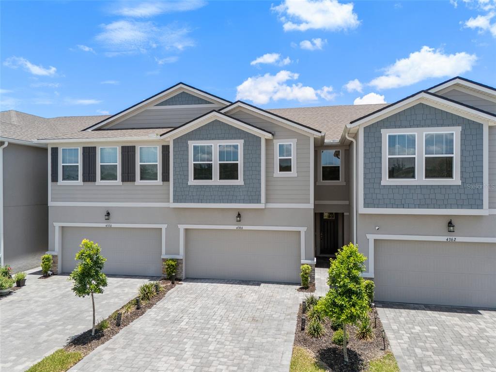 An exterior view of a multi-unit townhouse complex with gray siding, shingled roofs, and garages — 4366 CLOUD HOPPER WAY, LUTZ, FL