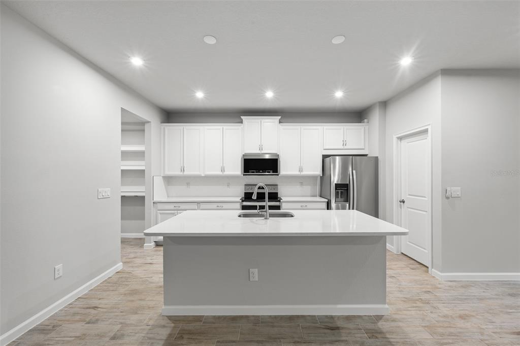 A modern kitchen features white cabinetry, stainless steel appliances, a center island, and tile flooring — 4366 CLOUD HOPPER WAY, LUTZ, FL