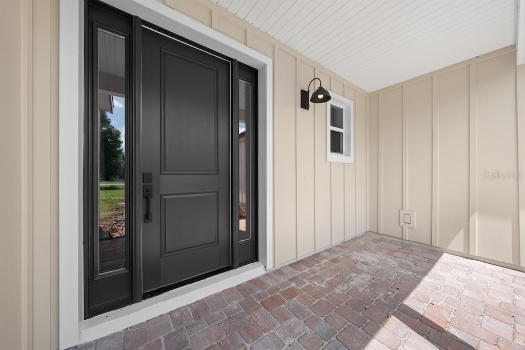A dark front door with sidelights sits on a brick porch with beige board-and-batten siding — 0 CORD AVENUE, ST CLOUD, FL