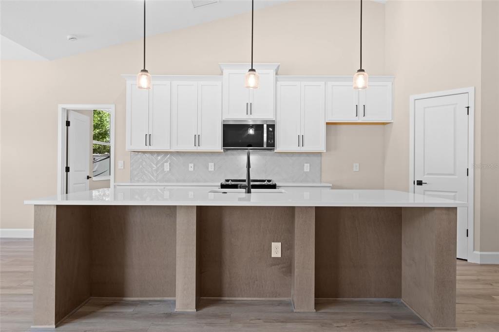 A modern kitchen features white cabinets, a large island with wood paneling, and pendant lighting — 0 CORD AVENUE, ST CLOUD, FL