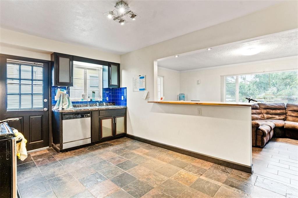 A kitchen with dark cabinets, blue tile backsplash, and a breakfast bar overlooking a living room — 912 DRUID ROAD E, CLEARWATER, FL