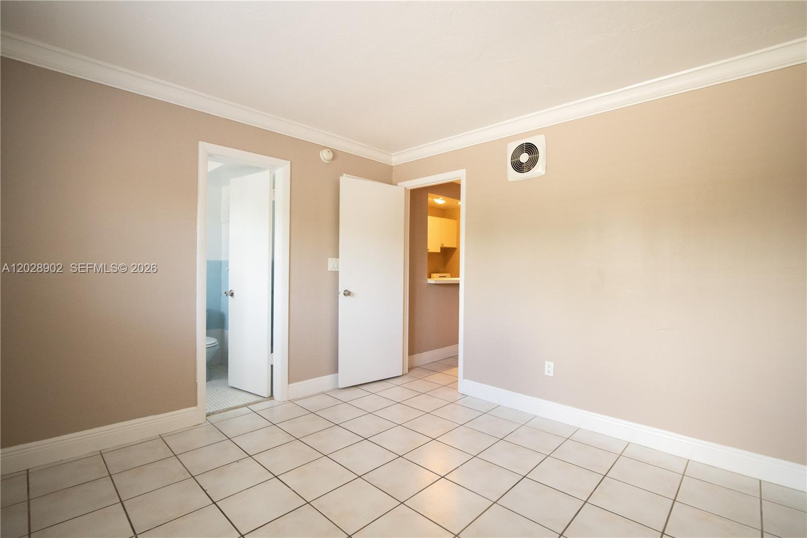 An interior room features beige walls, white tile flooring, two doorways, and a wall-mounted fan — 1014 Salzedo St # 101, Coral Gables FL 33134, CORAL GABLES, FL