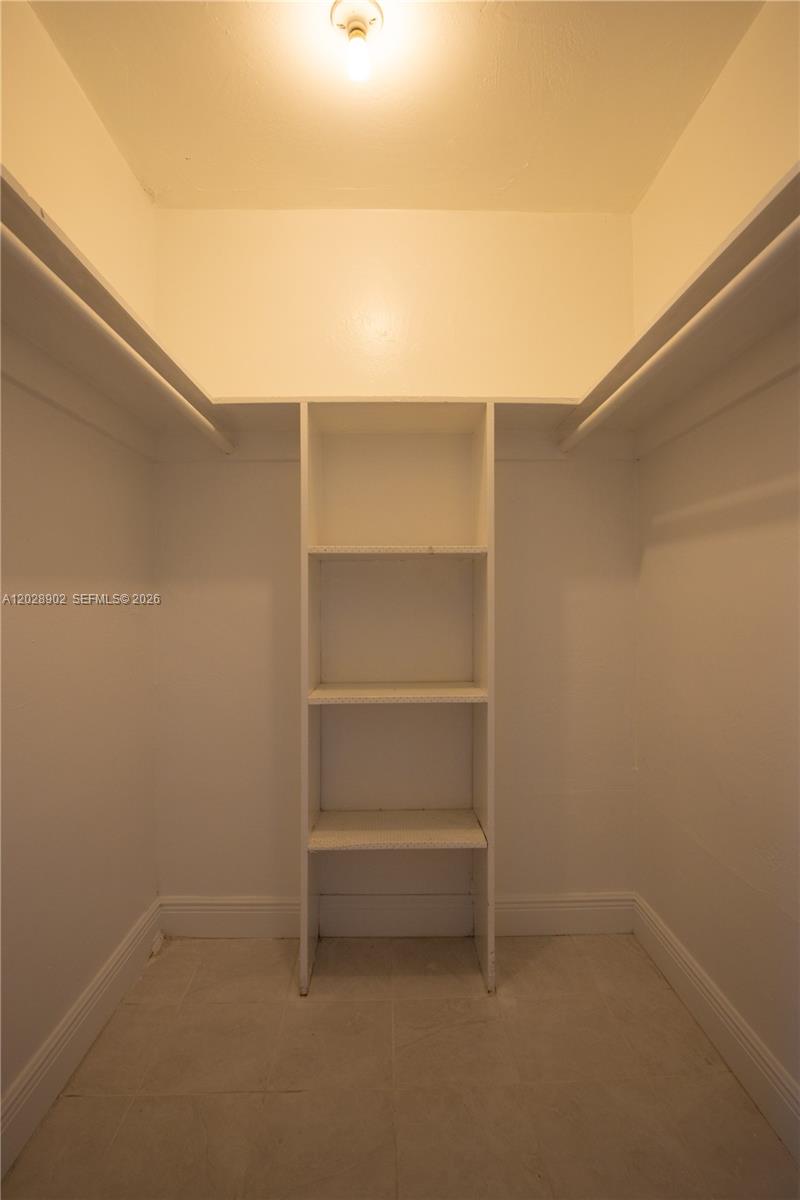 This walk-in closet features white walls, tile flooring, built-in shelving, and hanging rods — 1014 Salzedo St # 101, Coral Gables FL 33134, CORAL GABLES, FL