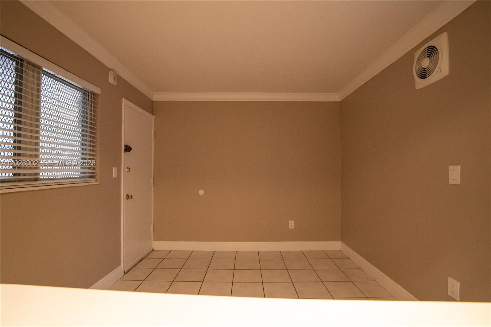 An empty room features beige walls, white tile flooring, a window with blinds, and a door — 1014 Salzedo St # 101, Coral Gables FL 33134, CORAL GABLES, FL
