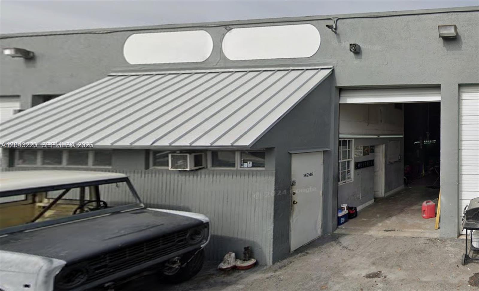 A gray industrial building exterior features a metal awning, a white door, and a vehicle — 14246 SW 139th Ct, Miami FL 33186, MIAMI, FL