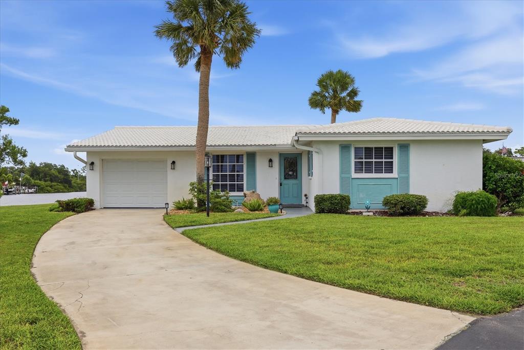 A single-story white house with a teal door, shutters, and a curved concrete driveway — 24 OAKWOOD DRIVE N UNIT 24, ENGLEWOOD, FL
