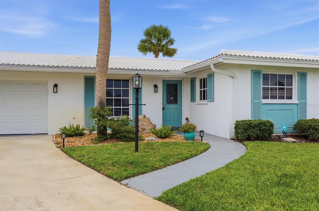 A white house with a teal front door, blue shutters, and a palm tree — 24 OAKWOOD DRIVE N UNIT 24, ENGLEWOOD, FL