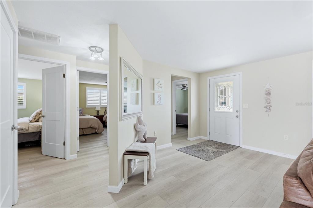 An entryway with light wood-look flooring, a white front door, and views into two bedrooms — 24 OAKWOOD DRIVE N UNIT 24, ENGLEWOOD, FL
