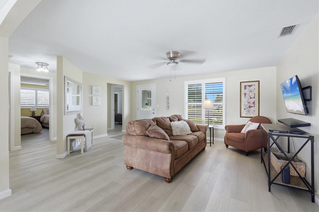 A living room features light-colored wood flooring, a brown sofa, an armchair, and a television — 24 OAKWOOD DRIVE N UNIT 24, ENGLEWOOD, FL