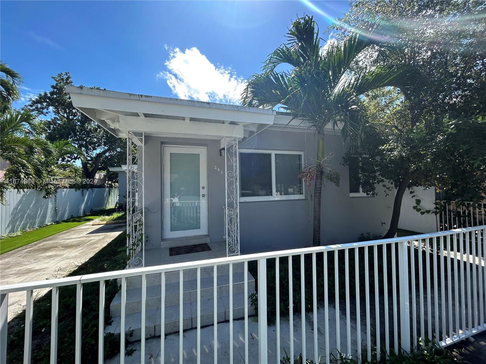 A small, gray, single-story house features a white front porch with decorative metal supports — 242 NE 55th Ter, Miami FL 33137, MIAMI, FL