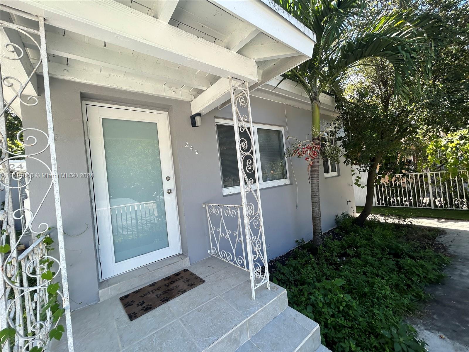 The exterior of a gray house features a white front door and decorative metal railings — 242 NE 55th Ter, Miami FL 33137, MIAMI, FL