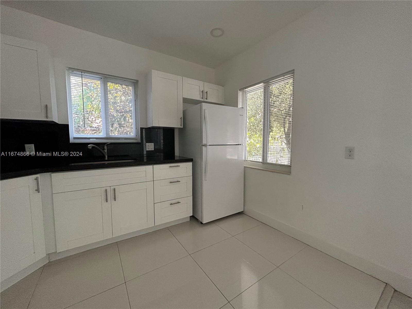 A kitchen features white cabinets, black countertops, a white refrigerator, and light tile flooring — 242 NE 55th Ter, Miami FL 33137, MIAMI, FL
