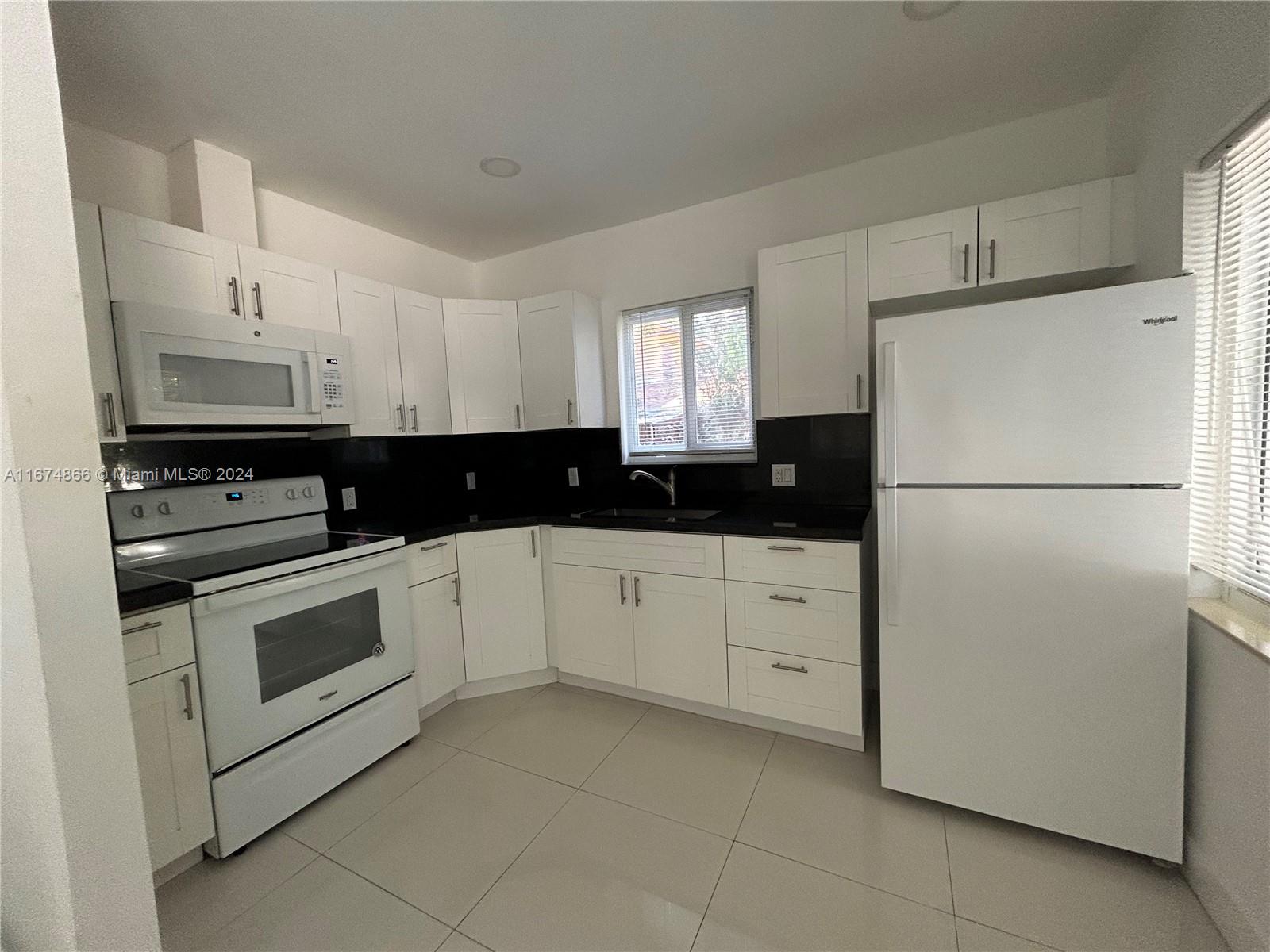 A kitchen features white cabinets, black countertops, a white stove, and a white refrigerator — 242 NE 55th Ter, Miami FL 33137, MIAMI, FL