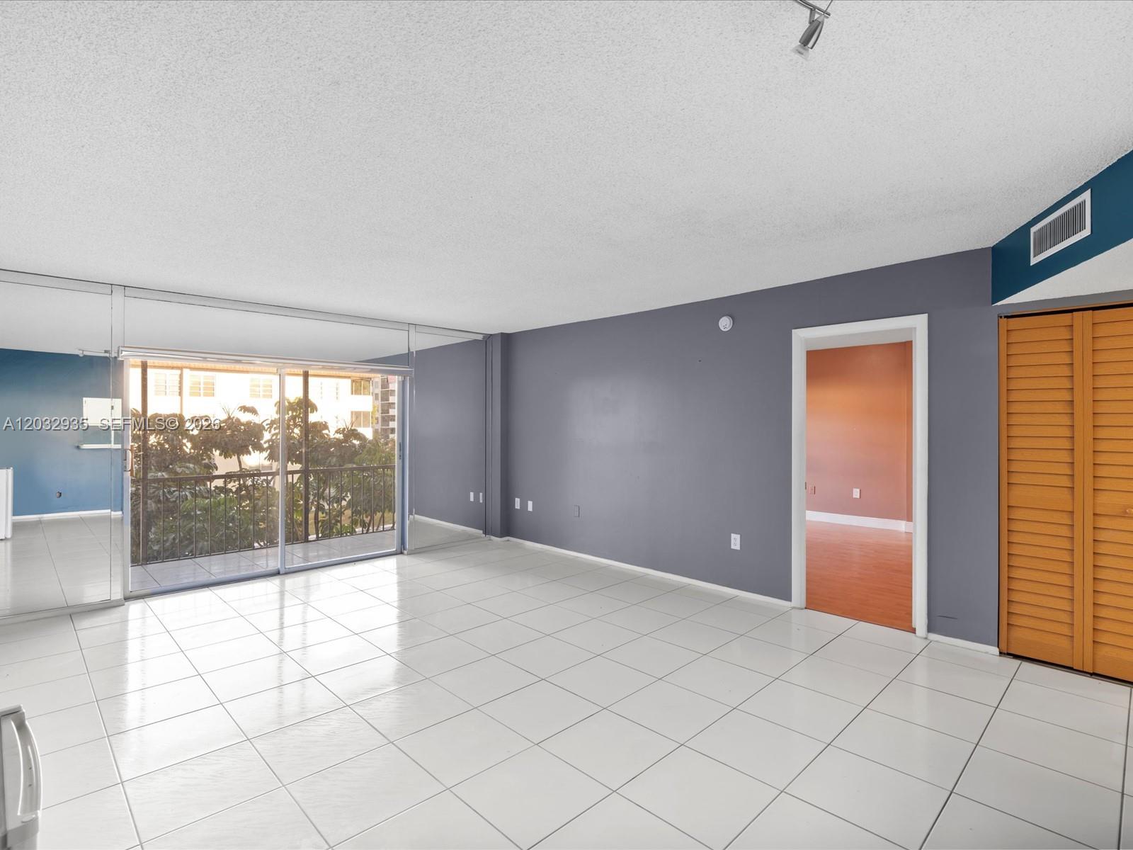 A living room with white tile floors, gray walls, mirrored panels, and a balcony door — 4172 Inverrary Dr # 306, Lauderhill FL 33319, LAUDERHILL, FL