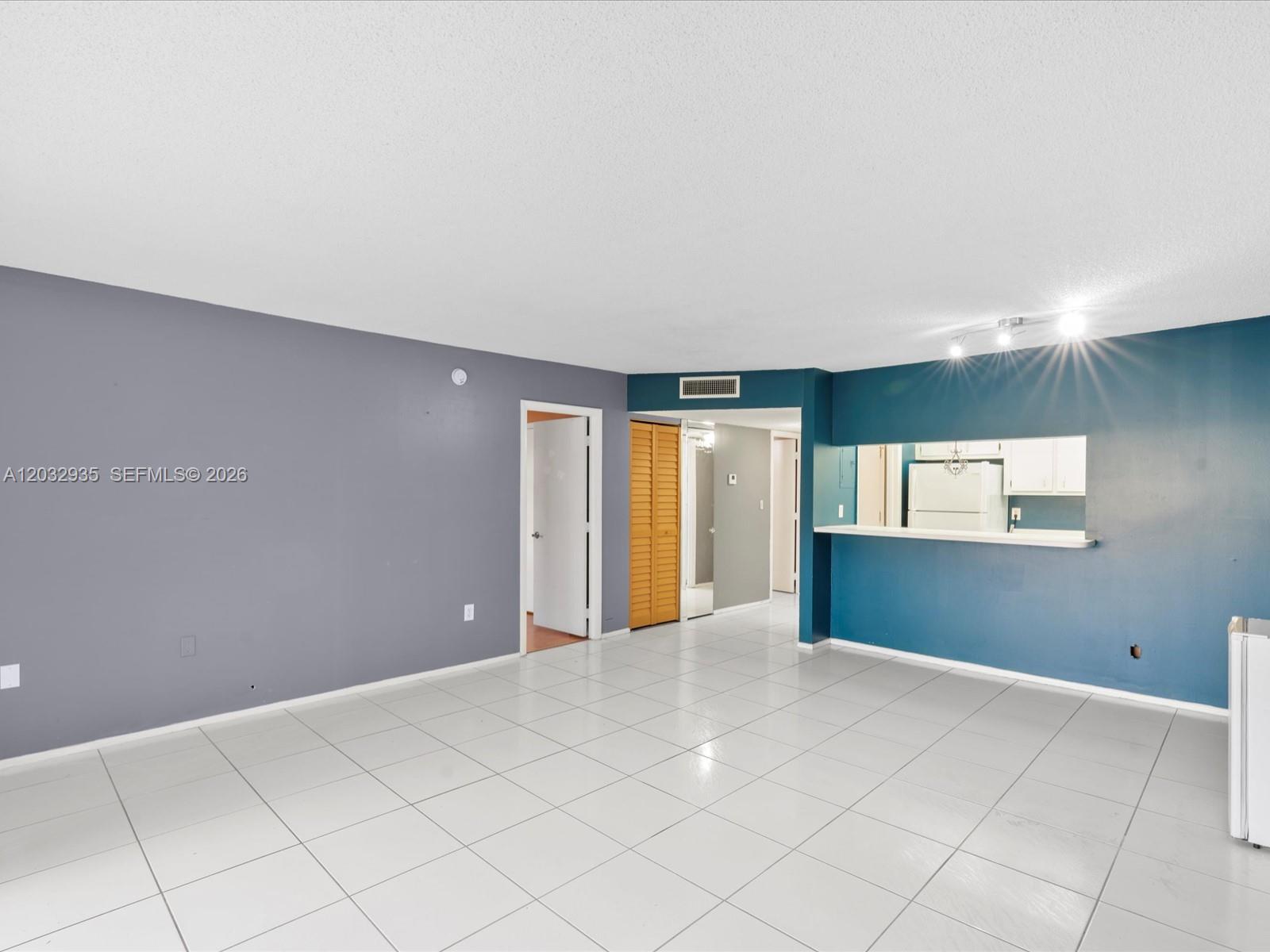 An empty living room features gray and blue walls, white tile flooring, and a kitchen pass-through — 4172 Inverrary Dr # 306, Lauderhill FL 33319, LAUDERHILL, FL
