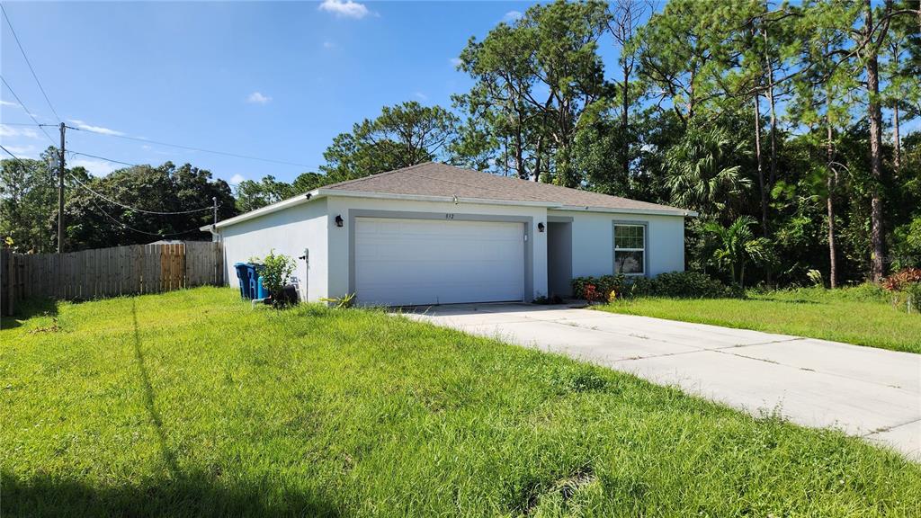 A single-story house with a white garage door, concrete driveway, and surrounding trees — 832 SORREL STREET NW, PALM BAY, FL