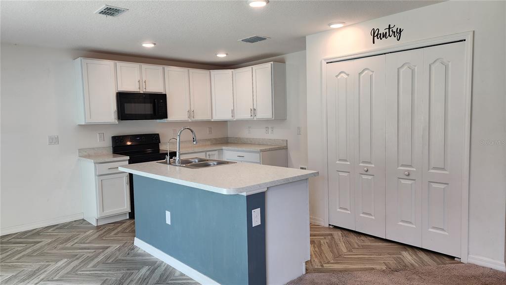 A kitchen features white cabinets, a blue island, a pantry, and light-colored countertops — 832 SORREL STREET NW, PALM BAY, FL